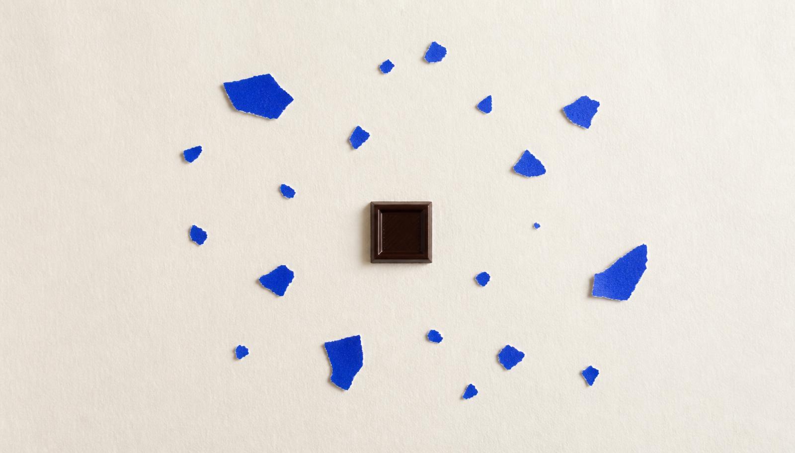 Un carré de chocolat entouré d'éclats de papier bleu, comme un nuage de notes de dégustation